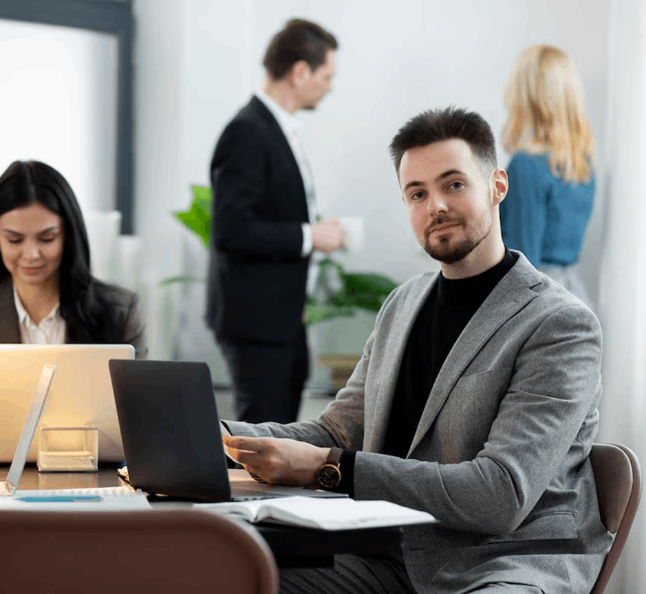 Mann mit Laptop an Tisch schaut in Kamera